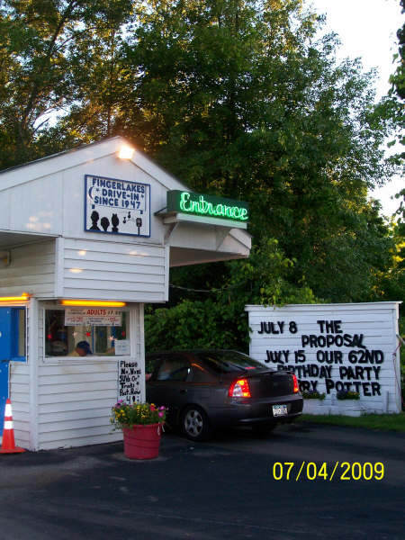 The Finger Lakes Drive-In entrance booth at dusk, hand-lettered "Fingerlakes Drive-In · Since 1947" with the green neon Entrance sign